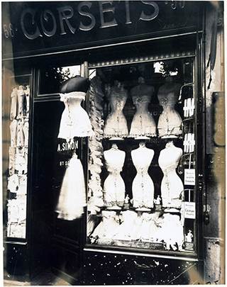 A shop window displaying rows of corsets on dress forms. 