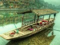 A Chinese wooden boat resting on still waters with reflection of ancient Chinese buildings along the riverbank.