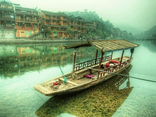 A Chinese wooden boat resting on still waters with reflection of ancient Chinese buildings along the riverbank.