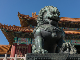 A Chinese lion sculpture in front of a Chinese palace-like building
