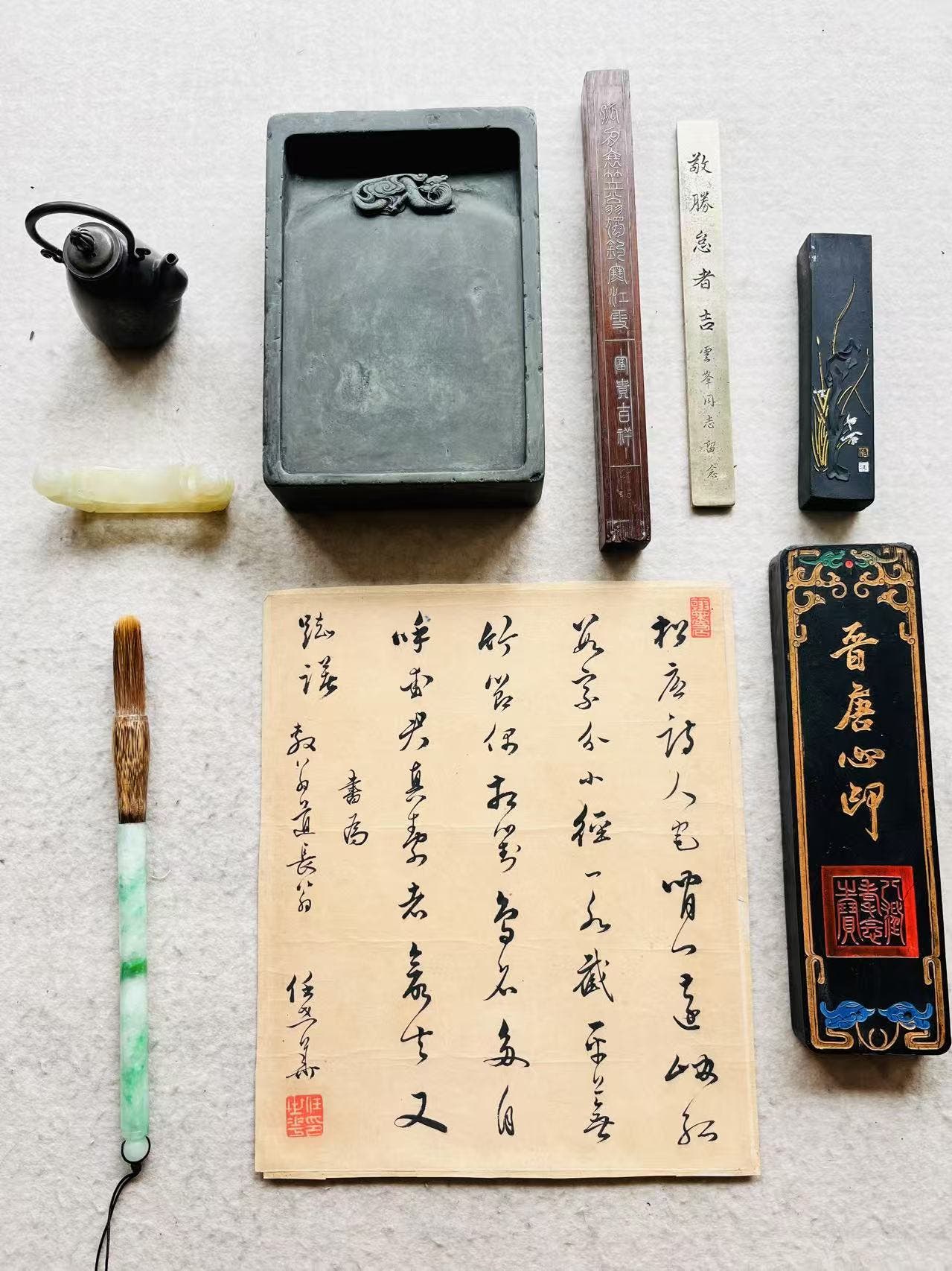 Chinese calligraphy tools laid out on a surface, including a brush, a brush rest, a piece of paper, an ink stone, and an ink