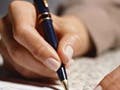 Photograph of a hand holding a pen and writing on a piece of paper.