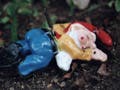 Ceramic figurine with red cap face down in the dirt with a knife in his back.