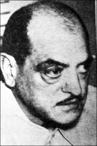 A black and white photograph of a man. He is balding and has a thin mustache.
