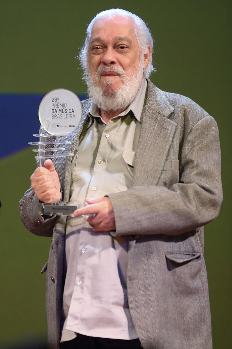An older man dressed holds an award on stage. 