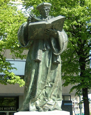 A statue of man wearing an elaborate robe and headwear, reading from a large book.