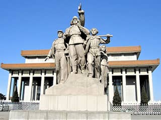 A statue featuring three men and one woman in battle garb sits in front of a modern, two-level building.