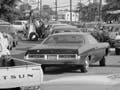 A black and white photo of cars and trucks lined up, surrounding a single gas pump.