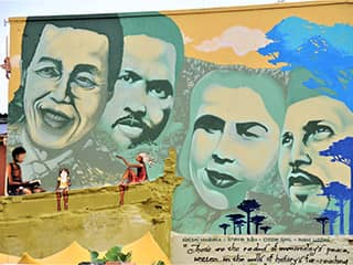 A colorful mural painted on the side of a building depicts the faces of three men and one woman.