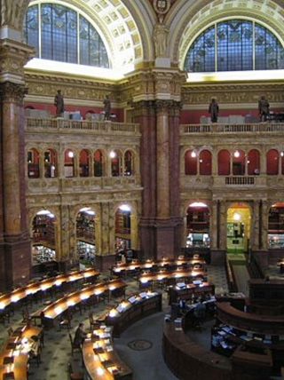Photo of a large reading room at the Library of Congress, with several circular rows of tables around a central main desk.