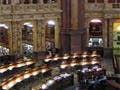 Photo of a large reading room at the Library of Congress, with several circular rows of tables around a central main desk.