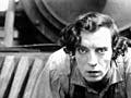 Photo of Buster Keaton crouched on the cowcatcher of a steam locomotive.