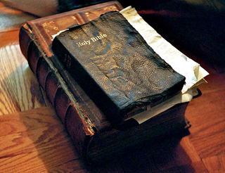 An old black leatherbound Bible atop a larger brown leatherbound book.