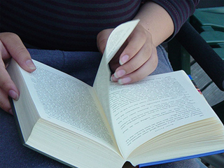 A book, open-faced, in a woman's lap, her hand turning the page.