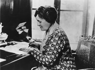 Photograph of Edith Wharton, writing while seated at a desk.
