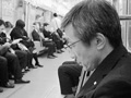 A man in a black coat sits on a subway and reads a book.