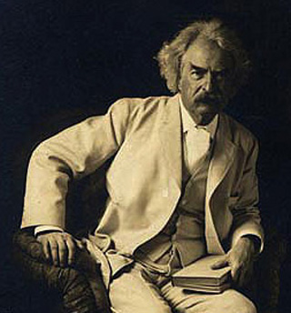 Photo of Mark Twain seated with a book in one hand.