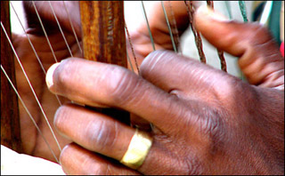 Closeup of two hands plucking kora strings.