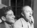 Candid photo: Bernstein's arm around Copland's shoulder; Copland singing.