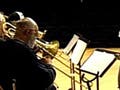 Photo of part of a large jazz ensemble on stage - saxophones and trombones - with conductor and composer out front.