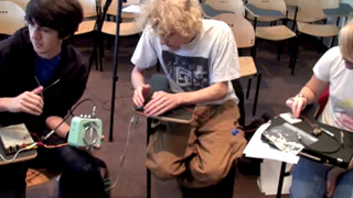 Still photo from video of class activity, showing three students working on a sonic circuit.