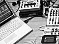 A photo of laptop computer, mixing board, iPod, two joystick controllers and several other electronic music devices arranged on a tabletop.