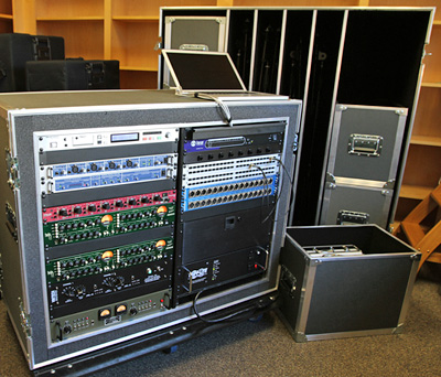 Photo of two large road cases, one with with rack-mounted electronics and a laptop computer, and the other containing several smaller cases with microphones, cables, etc.