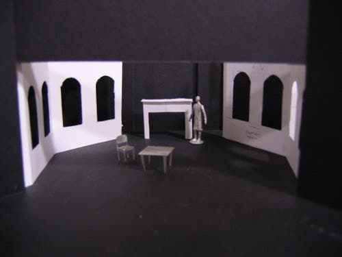 This room has large arch-topped picture windows on the right and left, with a fireplace dominating the wall in between, and a chair and table center stage.