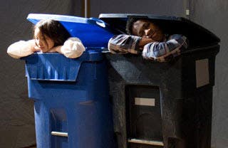 The heads of two people peek out from the top of garbage bins.