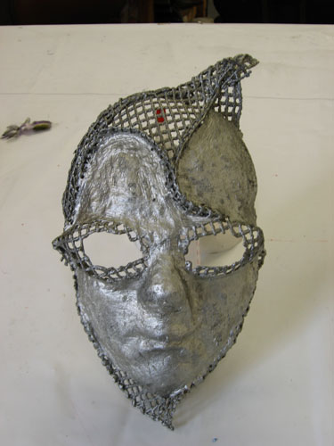 The eyeholes on this mask are shaped around cat-eye glasses, and the mesh section points aggressively at the top left before curving down to the left eyebrow and around the right side.