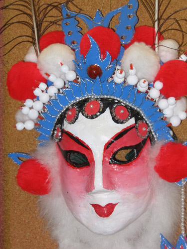Zooming in to show details of the face and crown, with decorative elements made of foam shapes, beads on pipe cleaners, rhinestones and glitter, and large red and white pompoms.