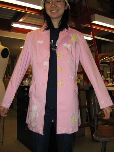 A pink thigh-length jacket features scattered clouds, a sheep holding the string of a balloon in its teeth, and white dot edging at the sleeves, pockets, and along the bottom hem.