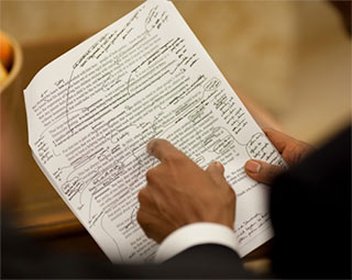A photo of President Obama's hand pointing to a draft of his healthcare speech, which is marked up with edits.