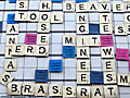 On the side of a building hang multi-colored squares, each with a letter or phrase on them, simulating a Scrabble game.