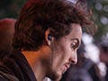 A curly-haired young man, with an earpiece hanging from his ear, types on a laptop.