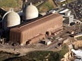 Photo of nuclear power plant on ocean shore, with two containment domes and a low rectangular building out front.