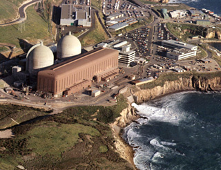 Photo of nuclear power plant on ocean shore, with two containment domes and a low rectangular building out front.