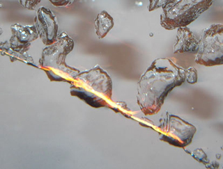Flames and bubbles surround a thin wire submerged in water.