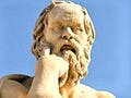 A marble statue of a seated, toga-wearing man with a furrowed brow and one hand resting on his chin.