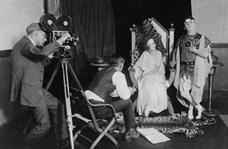 A photo of a cameraman, director and two actors on a set.