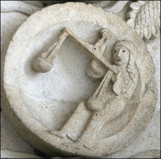 A photograph of a stone sculpture of Libra and her scales on Autun Cathedral.