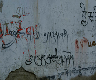 Tibetan graffiti on a crumbling plaster wall.