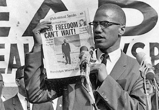 Malcolm X holds up a newspaper which reads, "Our Freedom Can't Wait"