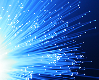 A bundle of blue optical fibers illuminated against a pitch black background.