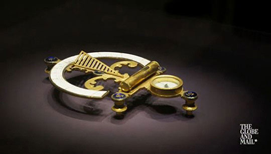 Still frame from a video showing a gold sextant on a gray background.