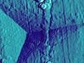 A sharp probe has left a triangular indentation in a surface, shown using scanning electron microscopy.