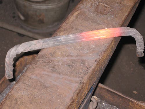 The red-hot bar shows grooves in two sides, all along the center between the bent ends.