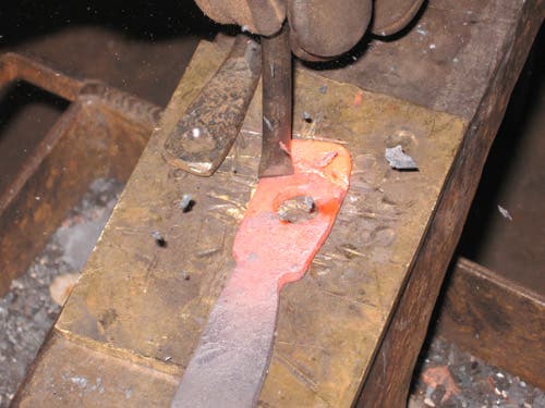 Zooming in, the red-hot metal is nearly cut through, so a bronze plate is placed under the workpiece with a hold-down.