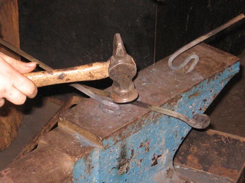 The twisted bar lies on the anvil face as a loop is made in one end of another bar.