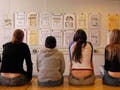 Six students sit on the edge of a table reviewing each others work.
